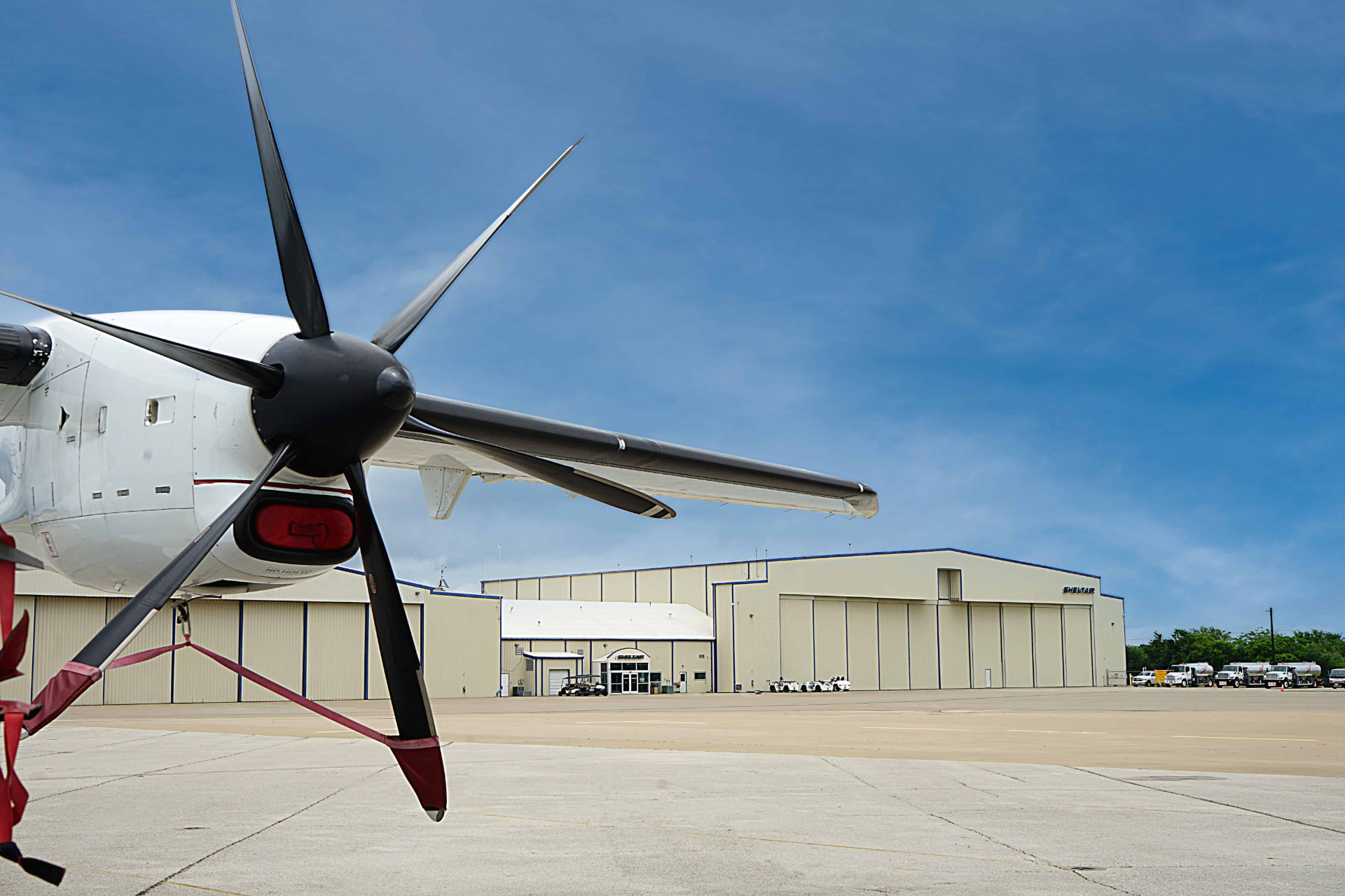Turboprop parked on the Sheltair ramp with the hangar line and fuel trucks behind it