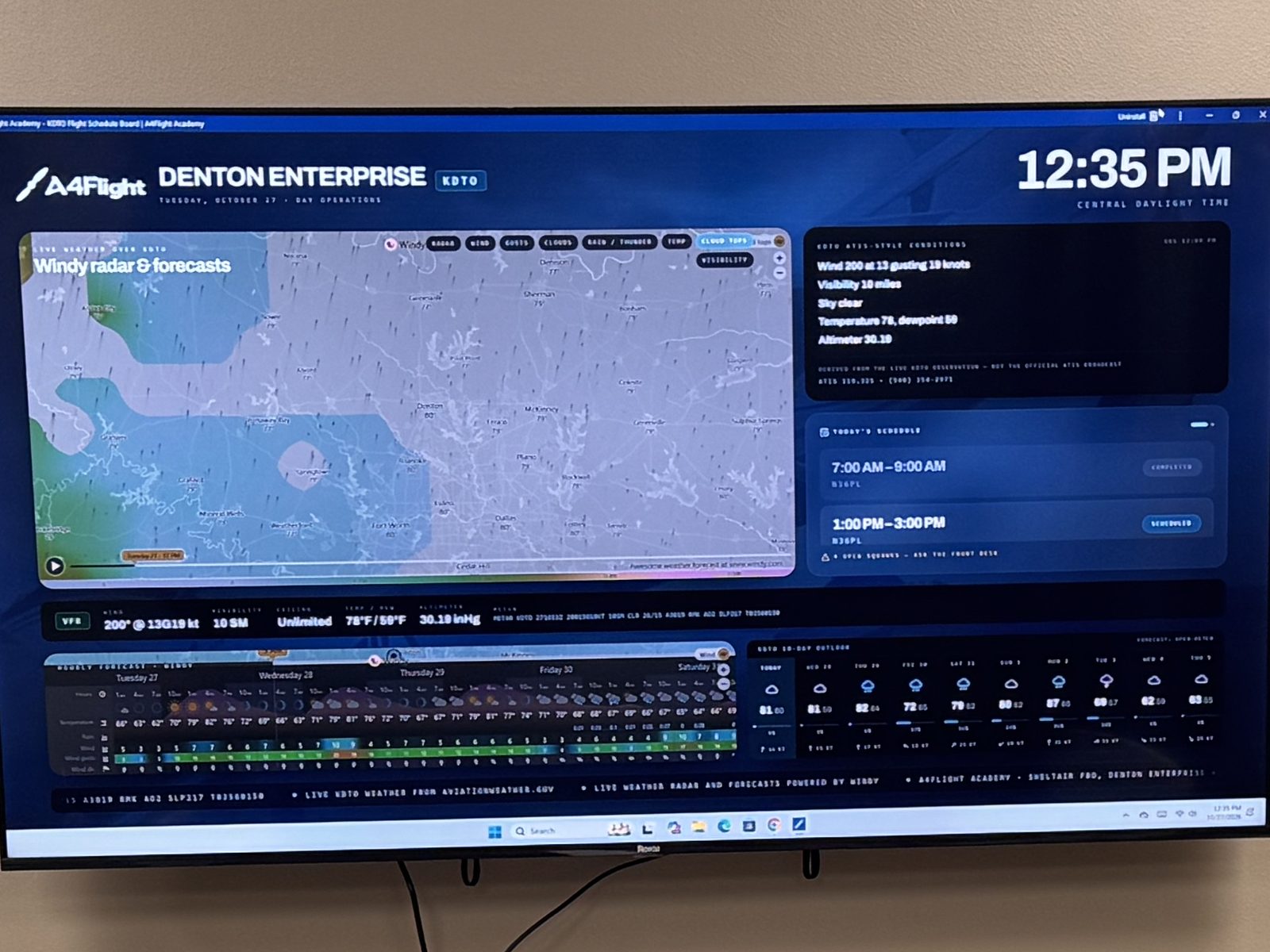 The A4Flight flight board on the briefing room wall, showing radar, weather and the day's schedule at Denton Enterprise Airport.
