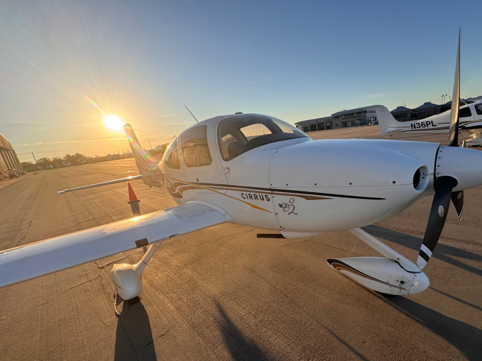 A Cirrus SR20 G2 parked on the ramp at Denton Enterprise Airport in early light, with the tower and hangar behind it.