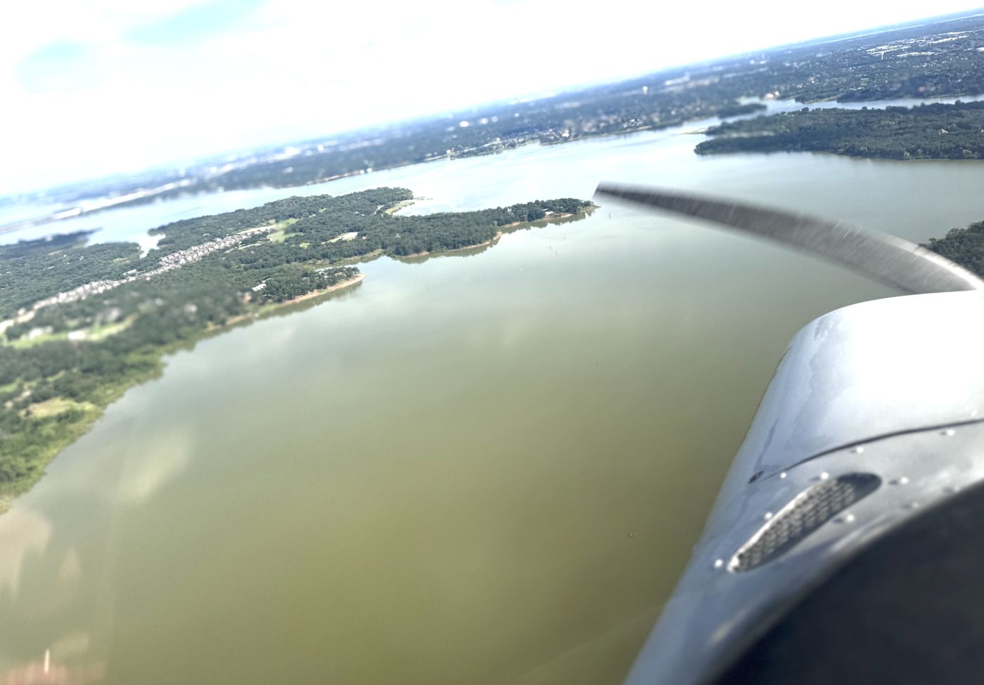 View over the spinning propeller and wing of a light aircraft over Texas lakes