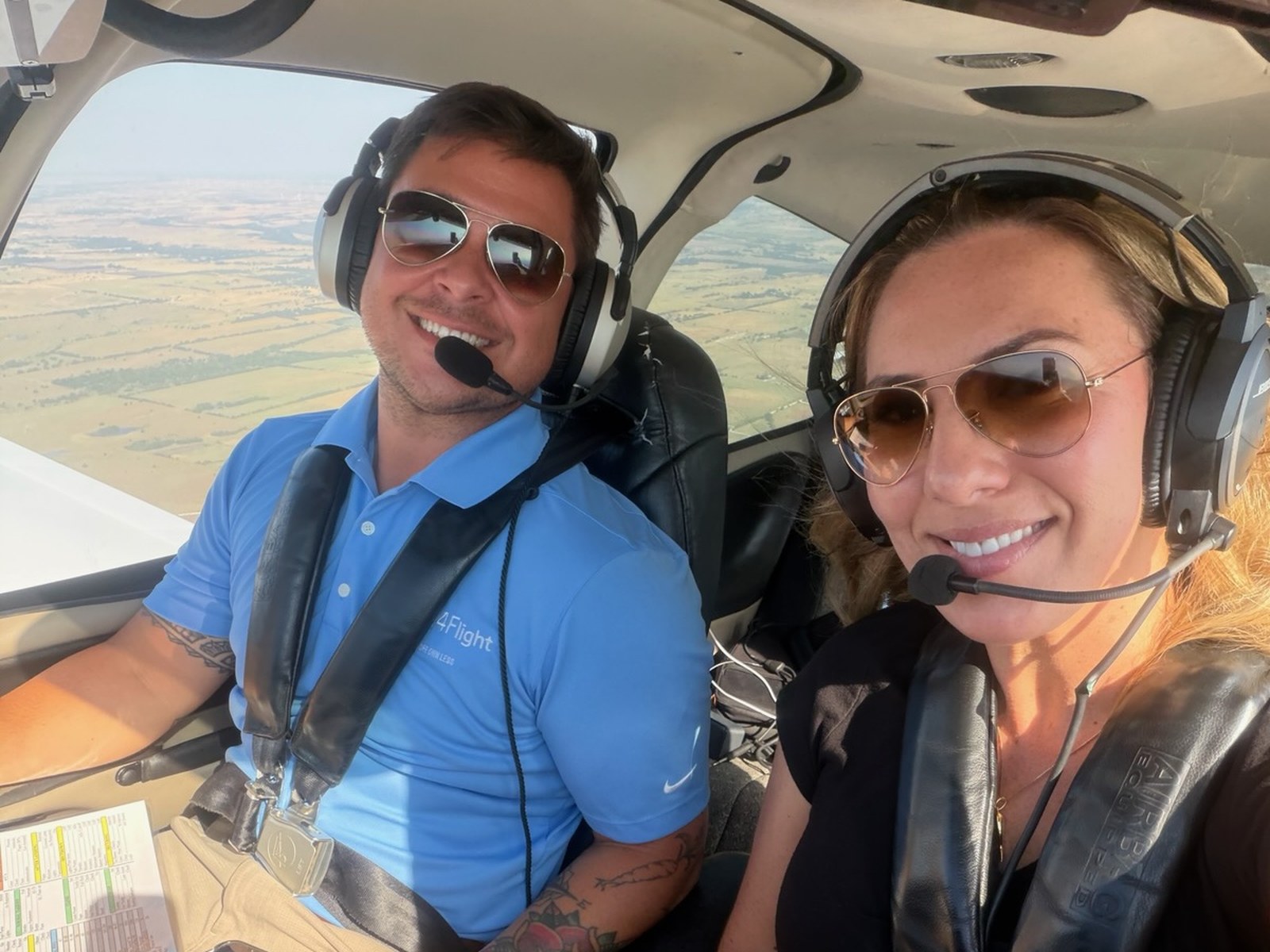 An A4Flight instructor and a student flying together in a Cirrus cockpit, both wearing headsets, farmland below.